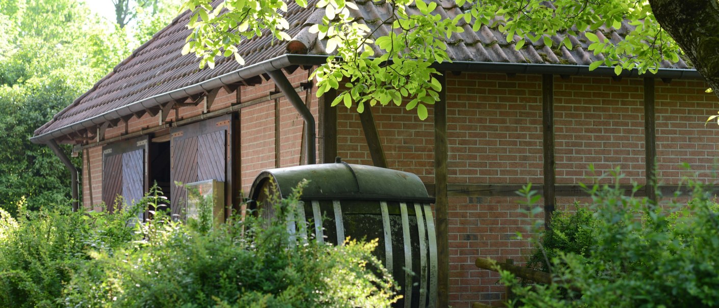 Brick building with wooden doors, surrounded by green bushes and trees. An old barrel stands in the foreground., &copy; Frank Nonnenmann