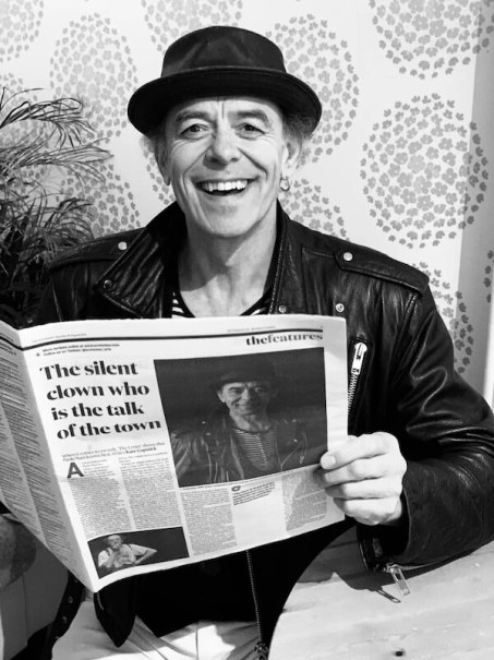 Ein Mann in Lederjacke und Hut lächelt, während er eine Zeitung mit dem Titel 'The silent clown who is the talk of the town' liest., © Theaterhaus Stuttgart e.V. Ein Mann in Lederjacke und Hut lächelt, während er eine Zeitung mit dem Titel 'The silent clown who is the talk of the town' liest., © Theaterhaus Stuttgart e.V.