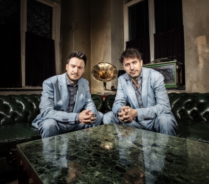 Zwei M&auml;nner stehen sich gegen&uuml;ber und halten gemeinsam eine Geige und eine Melodica. Sie schauen sich ernst an., &copy; Renitenztheater Stuttgart e.V.