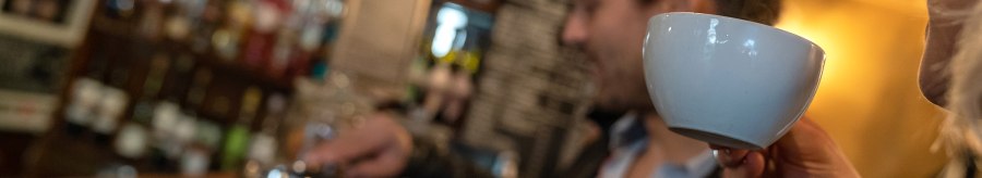 Two people in a caf&eacute;. One person is drinking from a cup while the other prepares coffee. Shelves with bottles can be seen in the background., &copy; Stuttgart Marketing  GmbH, Fotografin Martina Denker, post@denkerfotografie.de
