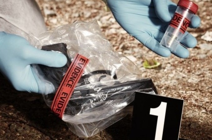 Tatortszene mit Beweismitteln: Eine Pistole in einer T&uuml;te und ein Probenr&ouml;hrchen werden von behandschuhten H&auml;nden untersucht, markiert mit Nummer 1., &copy; Cool-Tours StattReisen