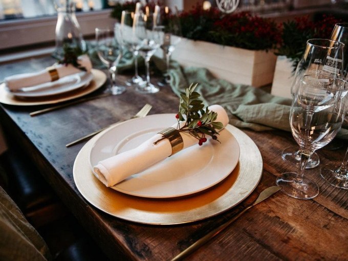 Elegante Tischdekoration mit goldenen Tellern, wei&szlig;en Servietten und gr&uuml;nen Zweigen auf einem Holztisch, umgeben von Weingl&auml;sern., &copy; Cool-Tours StattReisen