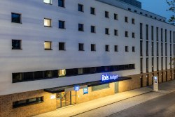 Außenansicht eines modernen Gebäudes bei Nacht, beleuchtet mit einem Ibis Budget Hotelschild. Mehrere Fenster sind sichtbar., © DQuadrat Living GmbH Außenansicht eines modernen Gebäudes bei Nacht, beleuchtet mit einem Ibis Budget Hotelschild. Mehrere Fenster sind sichtbar., © DQuadrat Living GmbH