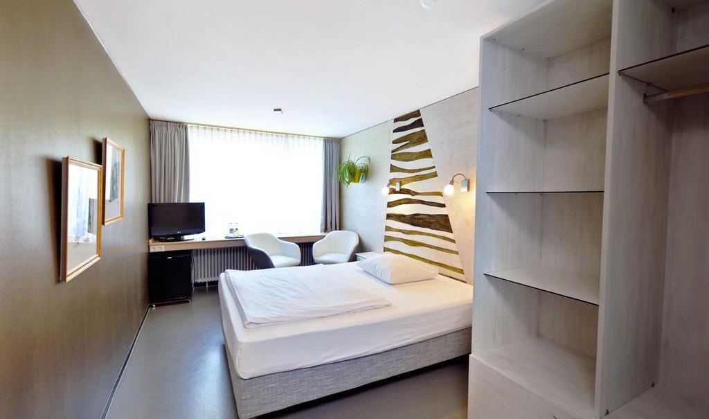 Ein modernes Einzelzimmer mit einem Bett, Schreibtisch, Fernseher und offener Garderobe. Die Wanddekoration ist stilvoll gestaltet., © Abalon Hotel Ideal Ein modernes Einzelzimmer mit einem Bett, Schreibtisch, Fernseher und offener Garderobe. Die Wanddekoration ist stilvoll gestaltet., © Abalon Hotel Ideal