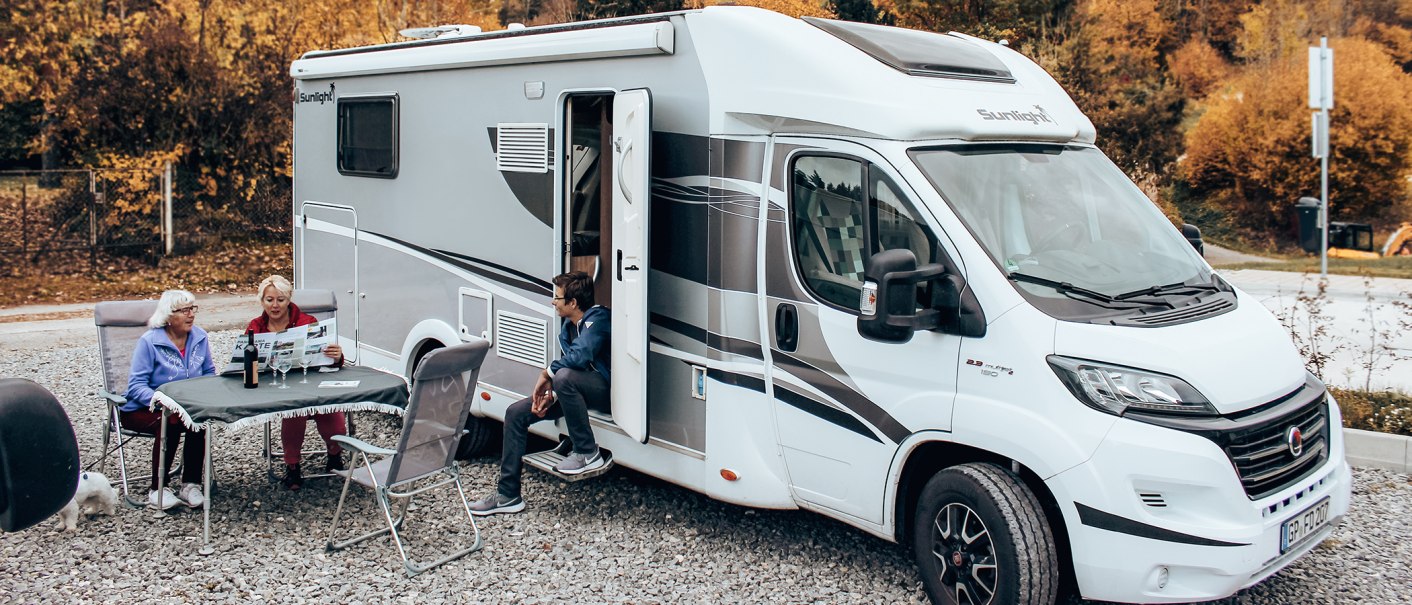 Ein Wohnmobil steht auf einem Stellplatz. Drei Personen sitzen davor an einem Tisch, ein Hund ist ebenfalls zu sehen. Herbstliche Bäume im Hintergrund., © Erlebnisregion Schwäbischer Albtrauf e.V.