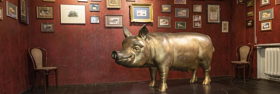 A room in the Stuttgart Pig Museum with a large pig sculpture and numerous framed pictures on a red wall., © Stuttgart-Marketing GmbH, Sarah Schmid