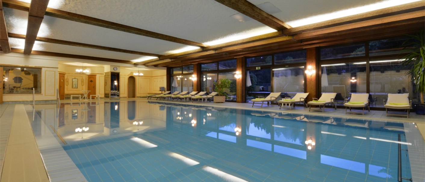 Elegant indoor pool with blue tiles, sun loungers and large windows. Wood paneling and warm lighting create a relaxing atmosphere., © TOMAS
