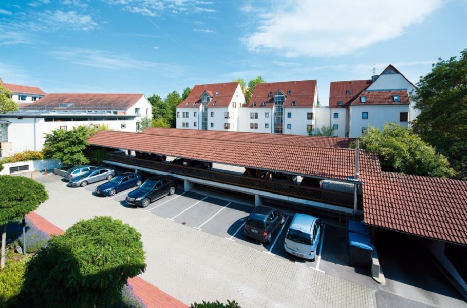 A parking lot with covered parking spaces, surrounded by residential buildings with red roofs and trees in the background., © Hotel Gasthof Hasen A parking lot with covered parking spaces, surrounded by residential buildings with red roofs and trees in the background., © Hotel Gasthof Hasen