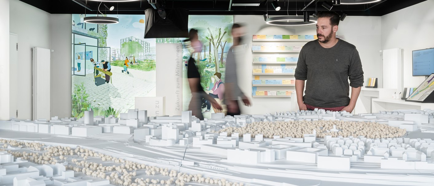 A man looks at an architectural model in an exhibition. Illustrations and notes can be seen on the wall in the background., © Dominique Brewing A man looks at an architectural model in an exhibition. Illustrations and notes can be seen on the wall in the background., © Dominique Brewing