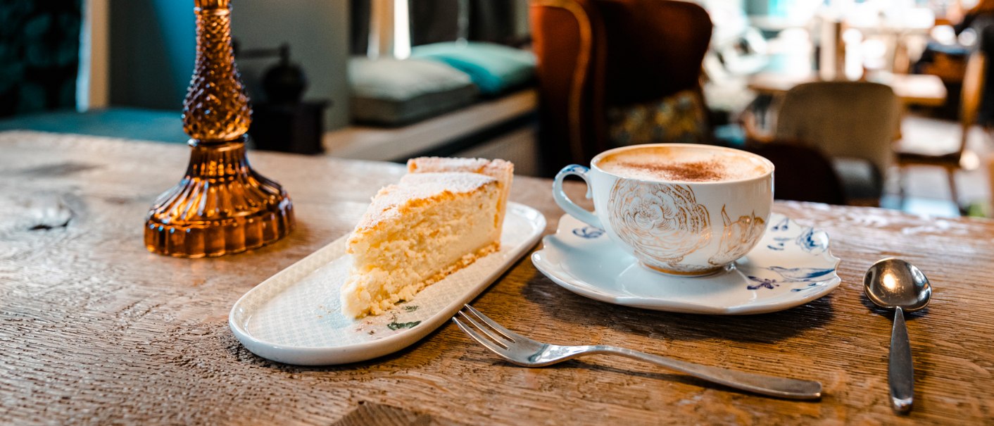 A piece of cake and a cup of coffee on a wooden table in a cozy café. Blurred furniture in the background., © SMG Stuttgart Marketing GmbH - Sarah Schmid