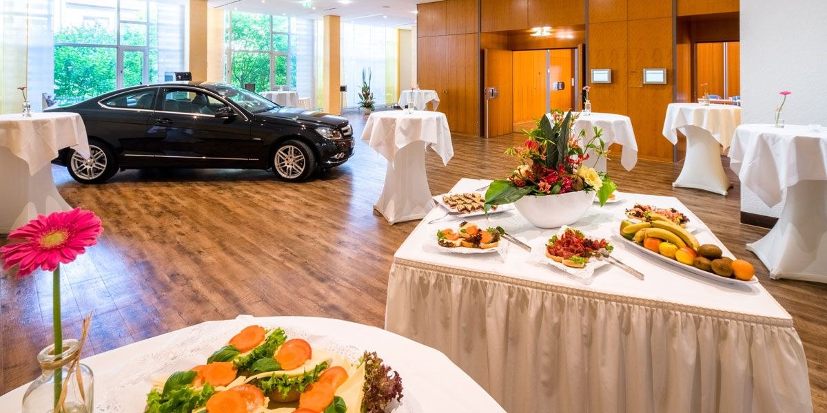 Elegantes Foyer mit schwarzem Auto, Stehtischen und Buffet mit Obst und Blumen., © Best Western Plus Hotel am Schlossberg