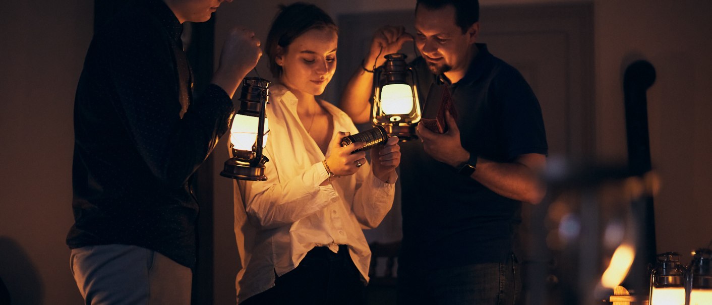 Drei Personen stehen in einem dunklen Raum und halten Laternen. Sie betrachten gemeinsam ein kleines Objekt, das eine von ihnen in der Hand hält., © Julia Ochs Drei Personen stehen in einem dunklen Raum und halten Laternen. Sie betrachten gemeinsam ein kleines Objekt, das eine von ihnen in der Hand hält., © Julia Ochs