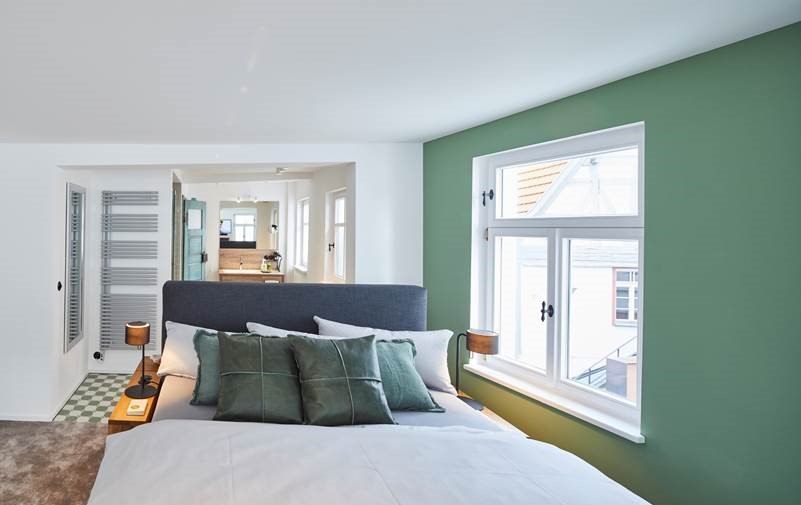 Modernes Schlafzimmer mit gr&uuml;n gestrichener Wand, gro&szlig;em Bett und Blick ins Badezimmer. Helle Fenster und stilvolle Einrichtung., &copy; Hotel Restaurant Bachofer
