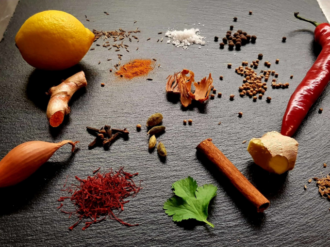 Zitrone, Ingwer, Chili, Schalotte, Zimtstange, Kardamom, Nelken, Safran, Petersilie und diverse Gew&uuml;rze auf dunkler Oberfl&auml;che arrangiert., &copy; Kultweine-Kochwelten-Kunst&uuml;cke - Kochschule Sonja Lenz