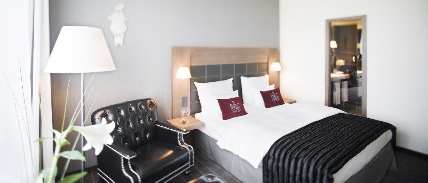 Elegantes Hotelzimmer mit Doppelbett, schwarzem Ledersessel, Stehlampe und dekorativen Kissen. Modernes Design mit neutralen Farben., © Mövenpick Hotel Stuttgart Airport Elegantes Hotelzimmer mit Doppelbett, schwarzem Ledersessel, Stehlampe und dekorativen Kissen. Modernes Design mit neutralen Farben., © Mövenpick Hotel Stuttgart Airport