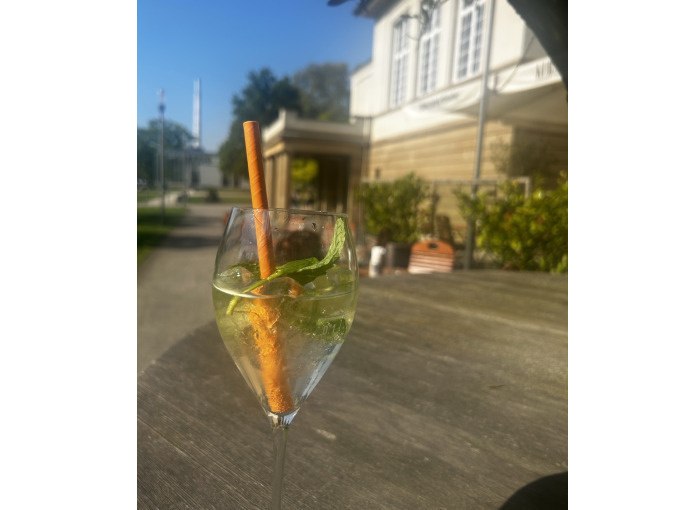 A glass with a drink, garnished with mint and a cinnamon stick, stands on an outdoor table in front of a building., © Cool-Tours StattReisen A glass with a drink, garnished with mint and a cinnamon stick, stands on an outdoor table in front of a building., © Cool-Tours StattReisen