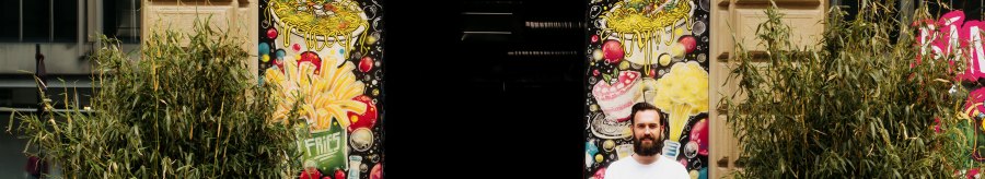 A man stands in front of the entrance to 'Banh Mi & Bubbles', surrounded by colorful graffiti and plants., &copy; Banh Mi & Bubbles Restaurant / Bar