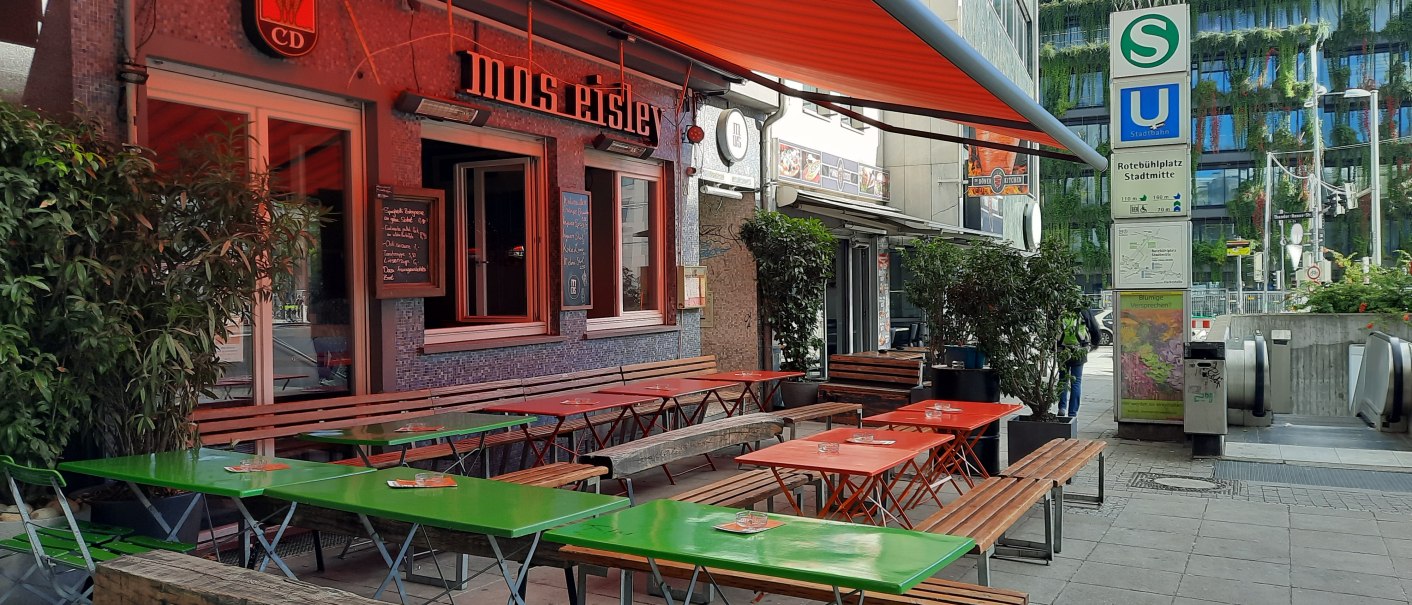 Außenbereich eines Cafés namens Mos Eisley mit bunten Tischen und Bänken. Daneben ein S- und U-Bahn-Schild am Rotebühlplatz Stadtmitte., © SMG Außenbereich eines Cafés namens Mos Eisley mit bunten Tischen und Bänken. Daneben ein S- und U-Bahn-Schild am Rotebühlplatz Stadtmitte., © SMG