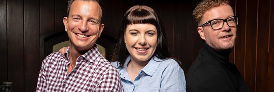Three people stand smiling next to each other in front of a wooden wall. They are wearing casual clothes and appear cheerful., © Zumbecher Three people stand smiling next to each other in front of a wooden wall. They are wearing casual clothes and appear cheerful., © Zumbecher