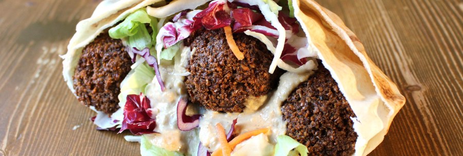 A falafel wrap with crispy falafel balls, fresh salad and sauce in a flatbread on a wooden table., © Vegi Stuttgart