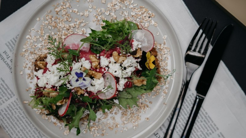 A decorative salad with radishes, nuts and edible flowers on a plate, served on a newspaper., © Fritz, Stuttgart
