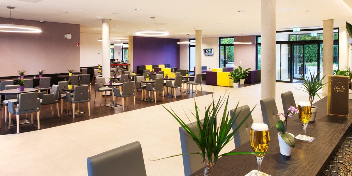Moderne Hotellobby mit grauen Stühlen, runden Tischen und Pflanzen. Im Hintergrund bunte Sitzgelegenheiten und große Fenster., © Star Inn Stuttgart Airport-Messe Moderne Hotellobby mit grauen Stühlen, runden Tischen und Pflanzen. Im Hintergrund bunte Sitzgelegenheiten und große Fenster., © Star Inn Stuttgart Airport-Messe