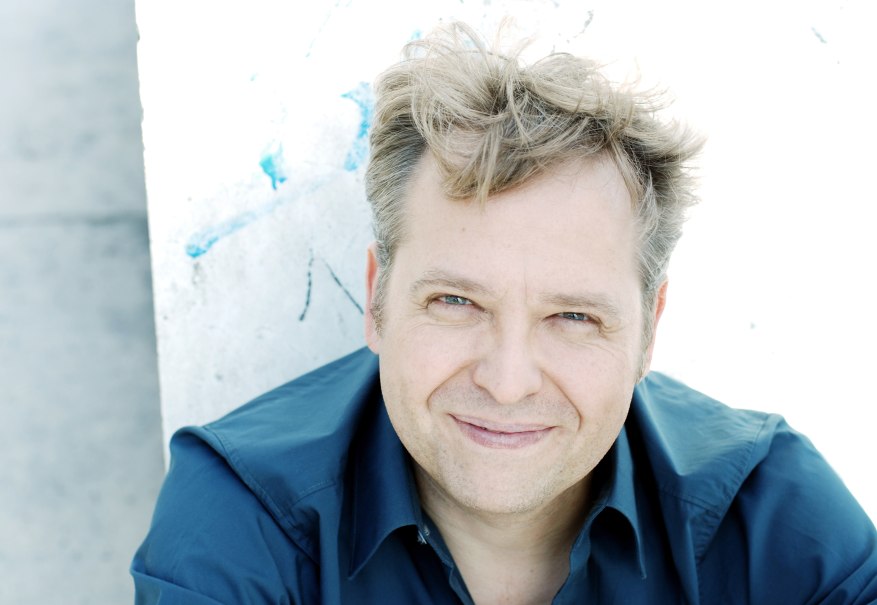 Ein Mann mit blonden Haaren und blauem Hemd l&auml;chelt in die Kamera. Der Hintergrund ist hell und leicht strukturiert., &copy; Soany Guigand