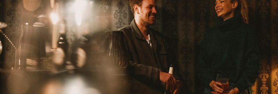 Two people are laughing in a cozy bar with subdued lighting and decorative wallpaper in the background., © Stuttgart Marketing GmbH, Fotograf Alwin Maigler, contact@alwinmaigler.com