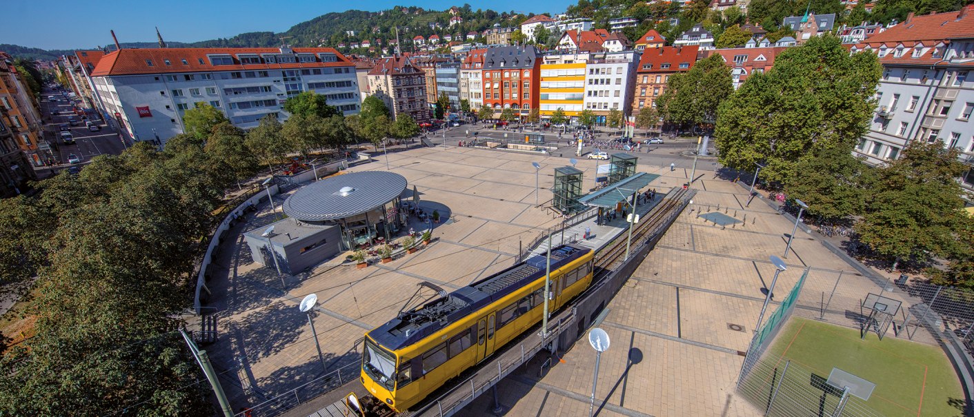 Luftaufnahme des Marienplatzes in Stuttgart. Eine gelbe Stra&szlig;enbahn f&auml;hrt vorbei, umgeben von B&auml;umen und Geb&auml;uden. Der Platz ist belebt und sonnig., &copy; Stuttgart-Marketing GmbH, Achim Mende