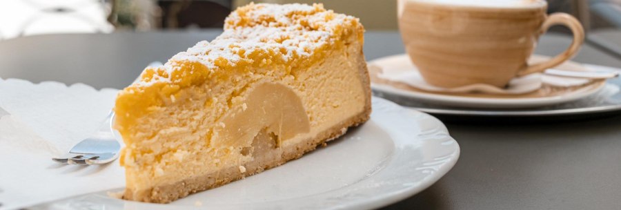 A slice of cake with powdered sugar on a plate, a cup of coffee next to it on a table in Caf&eacute; Schurr., &copy; SMG Stuttgart Marketing GmbH - Sarah Schmid