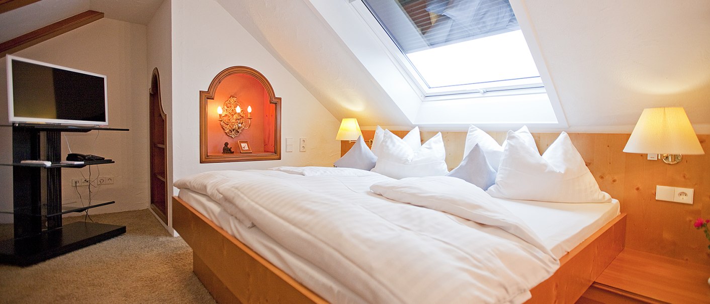 Gem&uuml;tliches Schlafzimmer mit Dachfenster, Doppelbett, Fernseher und warmem Licht. Holzm&ouml;bel und Teppichboden schaffen eine einladende Atmosph&auml;re., &copy; Hotel Krone