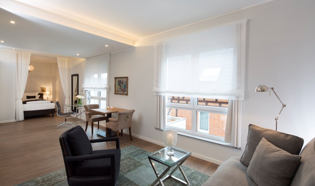 Modern suite with stylish sofa, table and chairs. Bright ambience with large windows and a cozy bed in the background., © Hotel LOGIS Modern suite with stylish sofa, table and chairs. Bright ambience with large windows and a cozy bed in the background., © Hotel LOGIS