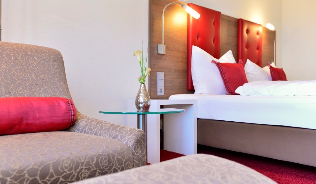 A stylishly furnished double room with a red carpet, a bed with red cushions and an armchair with a red cushion., © Hotel Fuchsen A stylishly furnished double room with a red carpet, a bed with red cushions and an armchair with a red cushion., © Hotel Fuchsen
