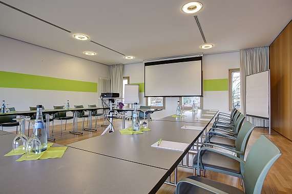 Moderner Tagungsraum mit Tischen, Stühlen, Projektor und Flipcharts. Helle Beleuchtung und grüne Akzente an den Wänden., © Centro Hotels