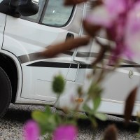 Weißes Wohnmobil auf Kiesplatz, im Vordergrund unscharfe Blumen. Seitliche Ansicht mit Fokus auf die Räder., © Erlebnisregion Schwäbischer Albtrauf e. V.