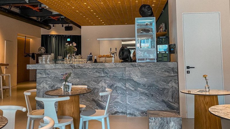 Modernes Café mit Marmortischen und einer stilvollen Theke. Dezente Beleuchtung und minimalistische Dekoration schaffen eine einladende Atmosphäre., © SMG Modernes Café mit Marmortischen und einer stilvollen Theke. Dezente Beleuchtung und minimalistische Dekoration schaffen eine einladende Atmosphäre., © SMG
