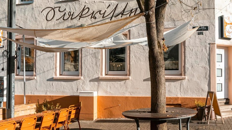 Ein Caf&eacute; mit Sonnensegeln und orangefarbenen St&uuml;hlen auf der Terrasse. Die Fassade ist wei&szlig; mit einem orangefarbenen Sockel., &copy; Stuttgart-Marketing GmbH, Sarah Schmid
