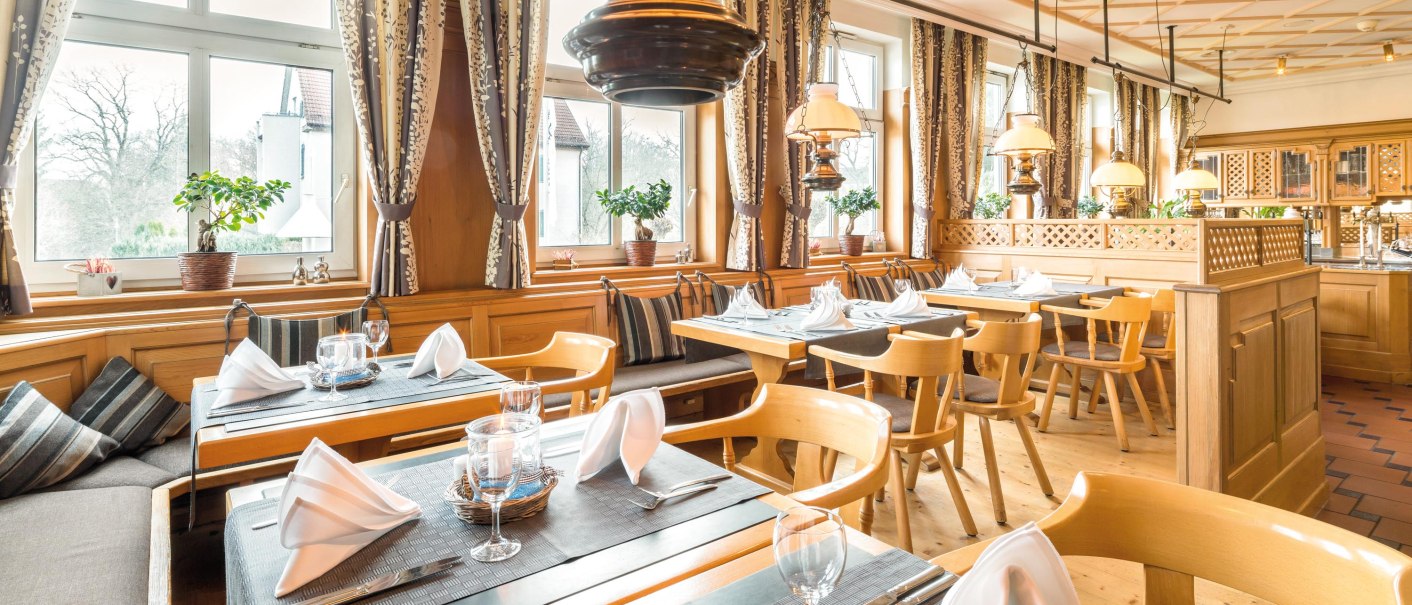 Gemütliches Restaurant mit Holzmöbeln, großen Fenstern und elegant gedeckten Tischen. Vorhänge und Pflanzen verleihen eine einladende Atmosphäre., © Seminaris Hotel Bad Boll