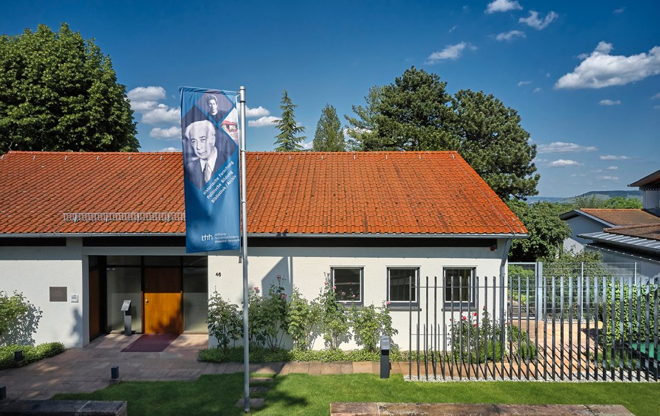 Das Theodor-Heuss-Haus mit rotem Ziegeldach und einer Fahne davor. Es ist von Bäumen umgeben und der Himmel ist blau mit wenigen Wolken., © Theodor-Heuss-Haus/Studio Olaf Becker
