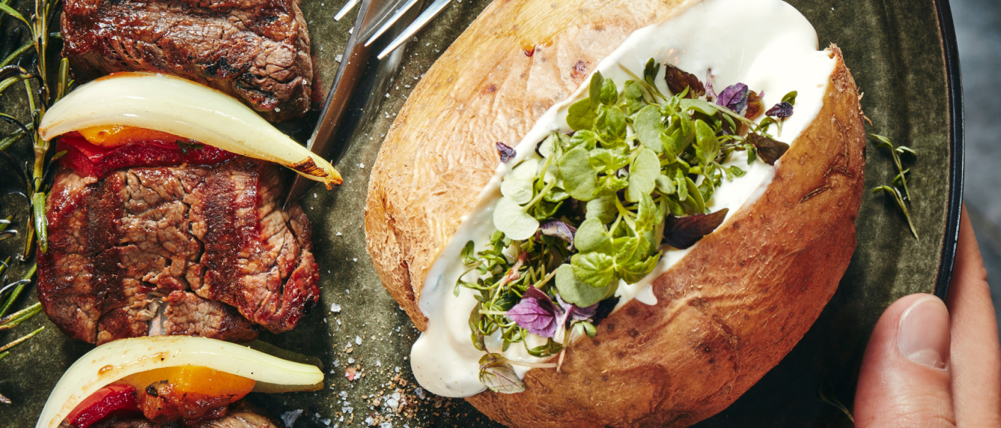 Grilled meat with peppers and onions, next to a baked potato with herbs and sour cream on a plate., © MAREDO Grilled meat with peppers and onions, next to a baked potato with herbs and sour cream on a plate., © MAREDO