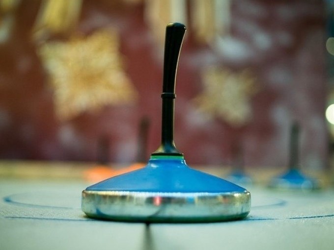 A blue curling stone stands on an ice rink, blurred shapes and colors can be seen in the background., © Cool-Tours StattReisen A blue curling stone stands on an ice rink, blurred shapes and colors can be seen in the background., © Cool-Tours StattReisen