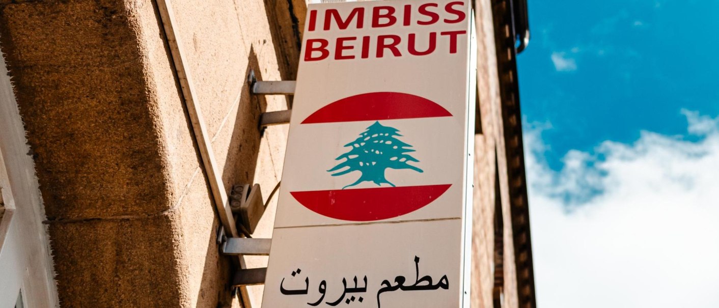 Schild eines Imbisses mit der Aufschrift 'Imbiss Beirut' und einem Zedernbaum-Logo, montiert an einer Gebäudewand., © Stuttgart-Marketing GmbH, Sarah Schmid Schild eines Imbisses mit der Aufschrift 'Imbiss Beirut' und einem Zedernbaum-Logo, montiert an einer Gebäudewand., © Stuttgart-Marketing GmbH, Sarah Schmid