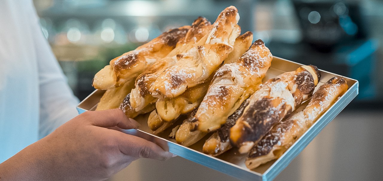 Eine Person präsentiert ein Tablett mit goldbraunen, frisch gebackenen Gebäckstangen in einem Café., © Café Justus, Stuttgart Eine Person präsentiert ein Tablett mit goldbraunen, frisch gebackenen Gebäckstangen in einem Café., © Café Justus, Stuttgart