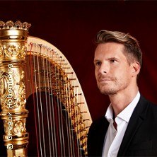Ein Mann in einem Anzug steht neben einer goldenen Harfe vor einem roten Hintergrund., © links im Bild Ein Mann in einem Anzug steht neben einer goldenen Harfe vor einem roten Hintergrund., © links im Bild