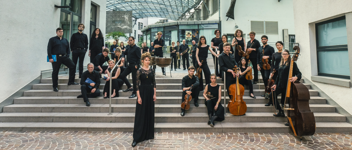 Eine Musikgruppe in schwarzer Kleidung posiert auf einer Treppe vor einem modernen Geb&auml;ude mit Glasdach., &copy; Martin F&ouml;rster