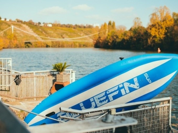 Blue and white SUP board on the riverbank, suspension bridge and autumnal landscape in the background., &copy; Cool-Tours StattReisen
