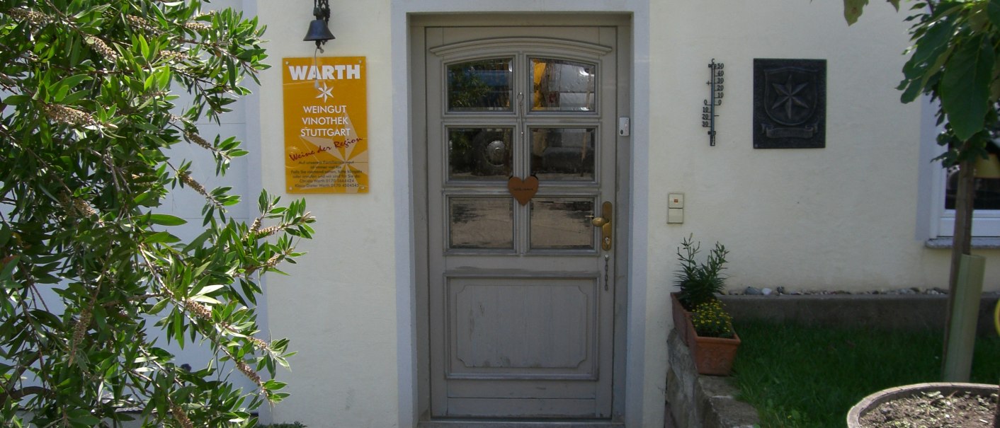 Eingang des Weinguts Warth mit gelbem Schild, Pflanzen und Holztür. Ein Thermometer und ein Wappen sind an der Wand angebracht., © Weingut Warth Eingang des Weinguts Warth mit gelbem Schild, Pflanzen und Holztür. Ein Thermometer und ein Wappen sind an der Wand angebracht., © Weingut Warth