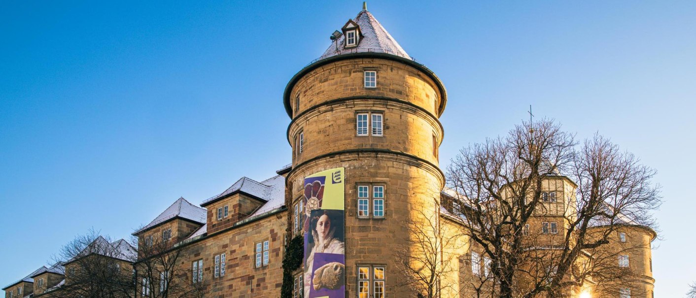 Das Alte Schloss in Stuttgart bei klarem Himmel. Ein Werbebanner schmückt die Fassade. Die Sonne scheint durch die kahlen Bäume., © Stuttgart-Marketing GmbH, Sarah Schmid Das Alte Schloss in Stuttgart bei klarem Himmel. Ein Werbebanner schmückt die Fassade. Die Sonne scheint durch die kahlen Bäume., © Stuttgart-Marketing GmbH, Sarah Schmid