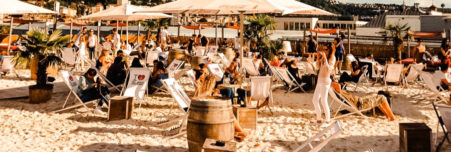 Strandbar mit Liegestühlen und Sonnenschirmen, umgeben von Palmen. Menschen entspannen sich unter blauem Himmel mit Wolken., © Sky Beach Strandbar mit Liegestühlen und Sonnenschirmen, umgeben von Palmen. Menschen entspannen sich unter blauem Himmel mit Wolken., © Sky Beach
