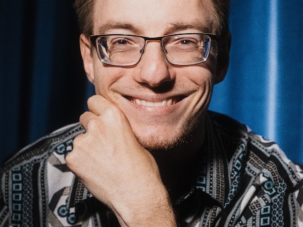 Ein Mann mit Brille und gemustertem Hemd lächelt in die Kamera. Im Hintergrund ist ein blauer Vorhang zu sehen., © Rosenau Kultur e.V. Ein Mann mit Brille und gemustertem Hemd lächelt in die Kamera. Im Hintergrund ist ein blauer Vorhang zu sehen., © Rosenau Kultur e.V.